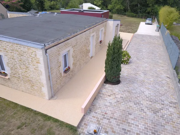 Maison avec cheminement en moquette de pierre beige, vue drone